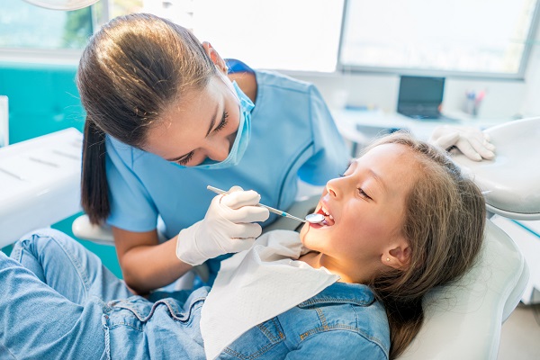A dentist is examining a kid's mouth with a dental explorer tool at the dental hospital, the background is surrounded by dental equipment.