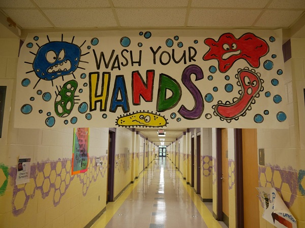 Empty school corridor with a hanging "Wash your hands" poster with viruses like figures drawn in bright colors , emphasizing covid 19 safety guidelines.